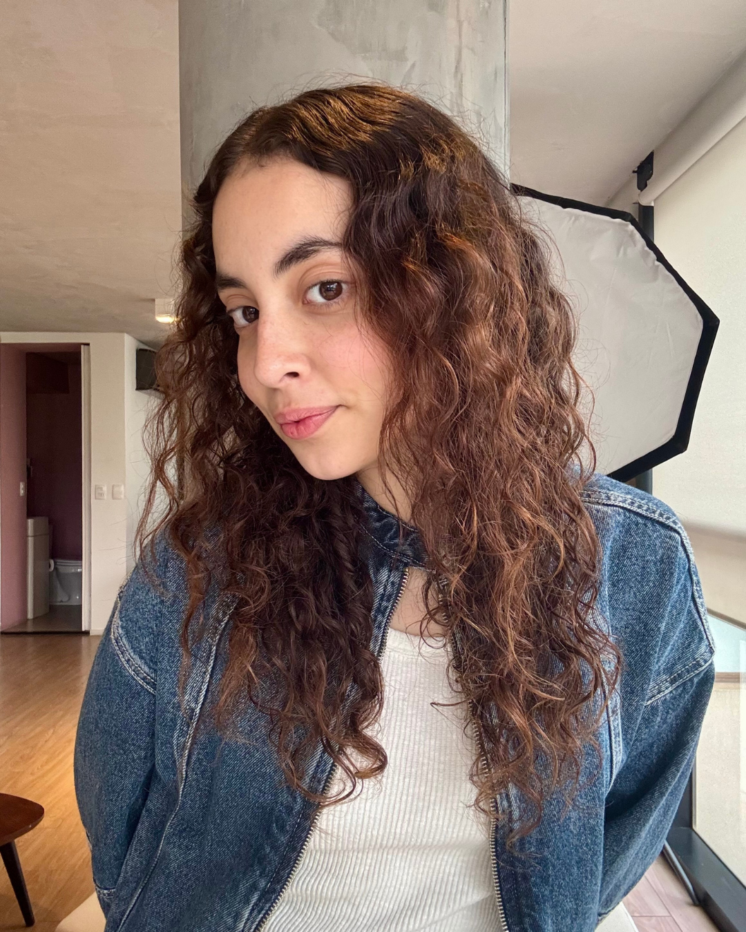 Modelo com cabelo cacheado solto e volumoso, veste jaqueta jeans azul oversized com rotina para cabelo cacheado por menos de 200 reais