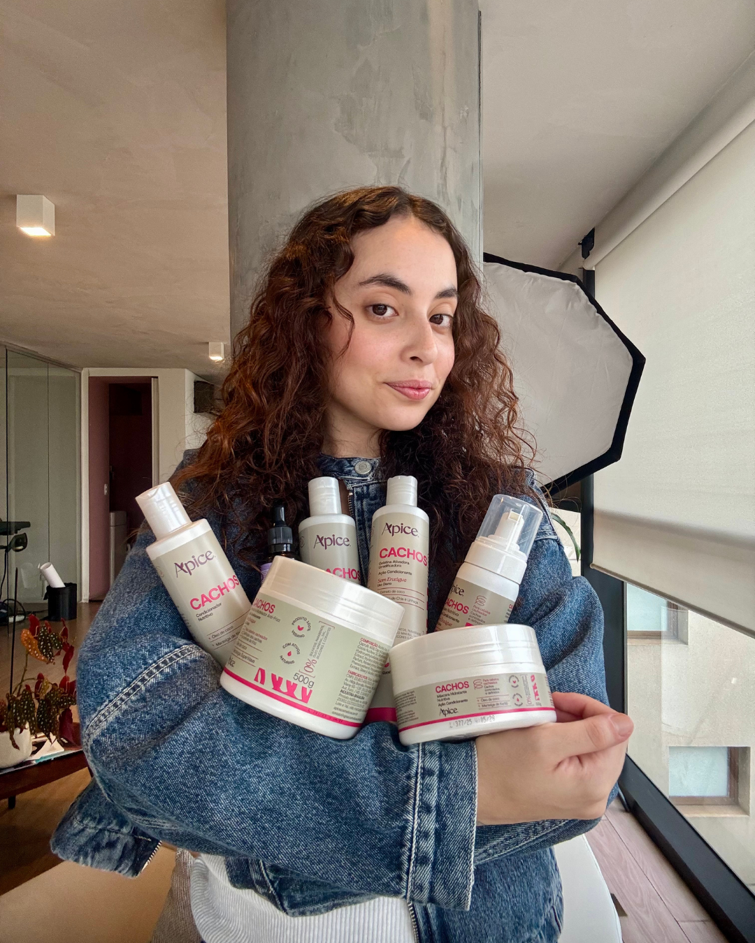 Mulher de cabelo cacheado abraça produtos Apice para rotina para cabelo cacheado por menos de 200 reais, vestindo jaqueta