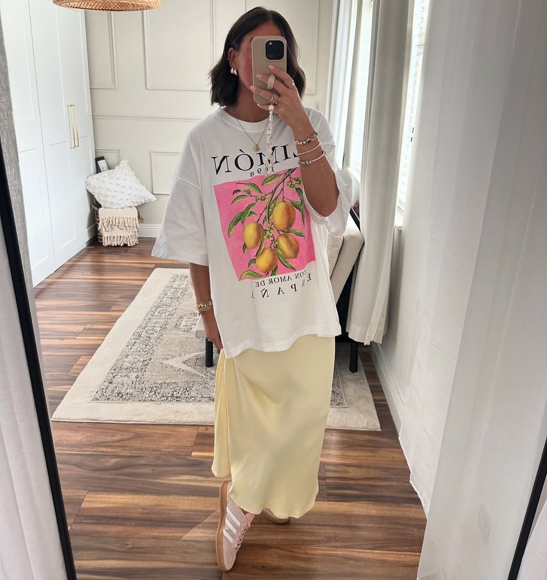 Modelo com camiseta branca oversized, saia amarela fluida e Adidas Sambae rosa com branco
