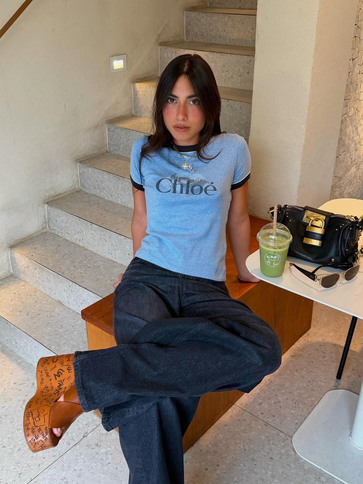 Modelo senta com postura relaxada e confiante usando sandálias da moda do verão 2026 em plataforma marrom com grafismos,