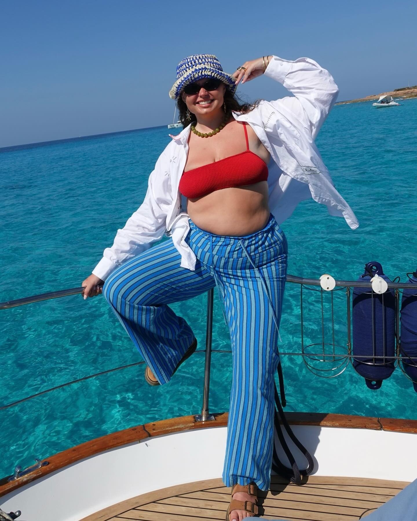 Modelo posa alegre em barco com sandálias da moda do verão 2026 em couro caramelo, combinando conforto e estilo casual.