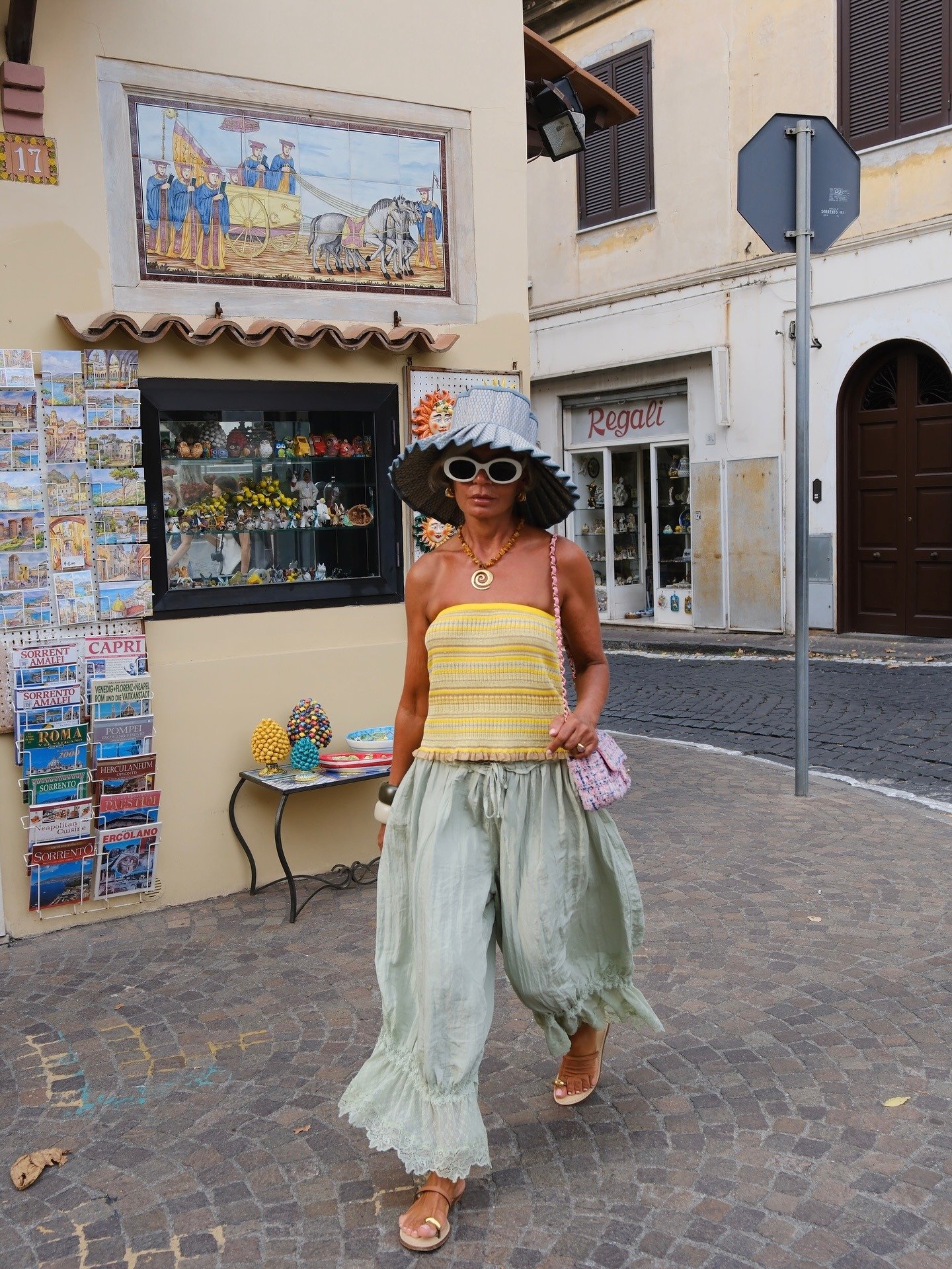 Mulher caminha confiante com sandálias da moda do verão 2026 em tiras finas bege, combinando top amarelo e calça ampla verde