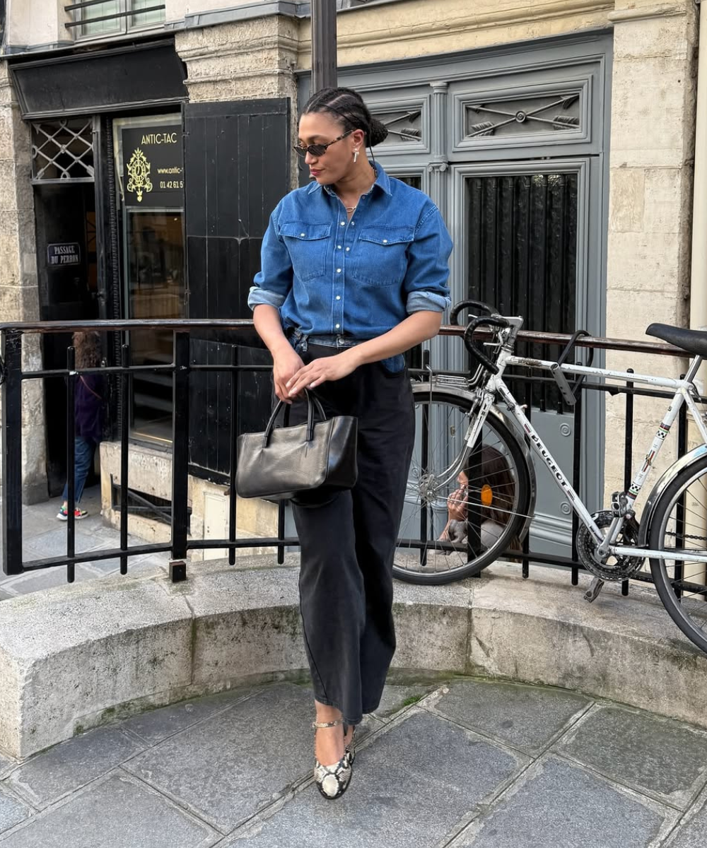 Modelo posa com camisa jeans azul, calça preta ampla e sapatos estampados tendência em animal print, combinando elegância