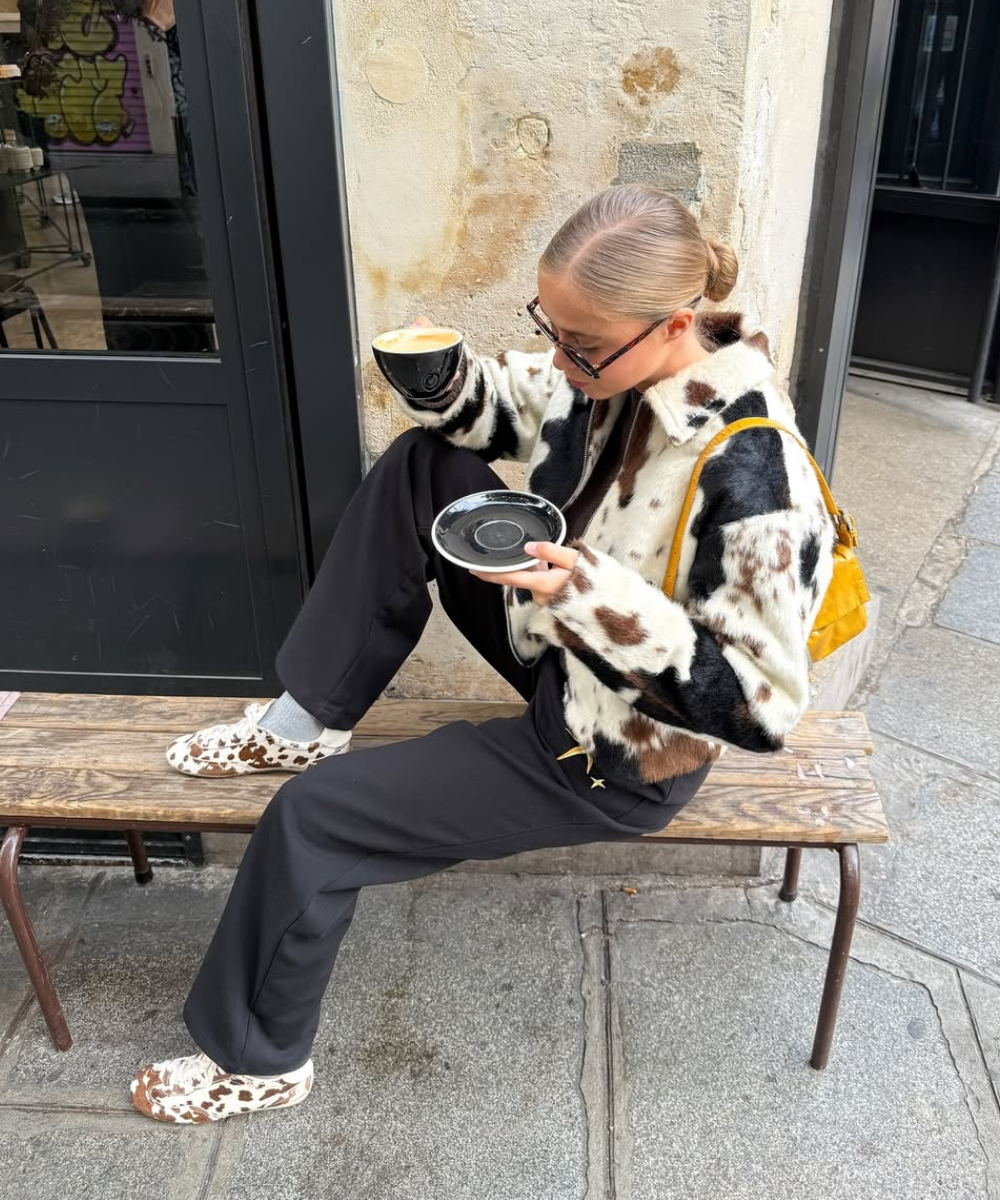 Modelo senta casualmente em banco rústico usando sapatos estampados tendência de animal print em tons marrom e branco,