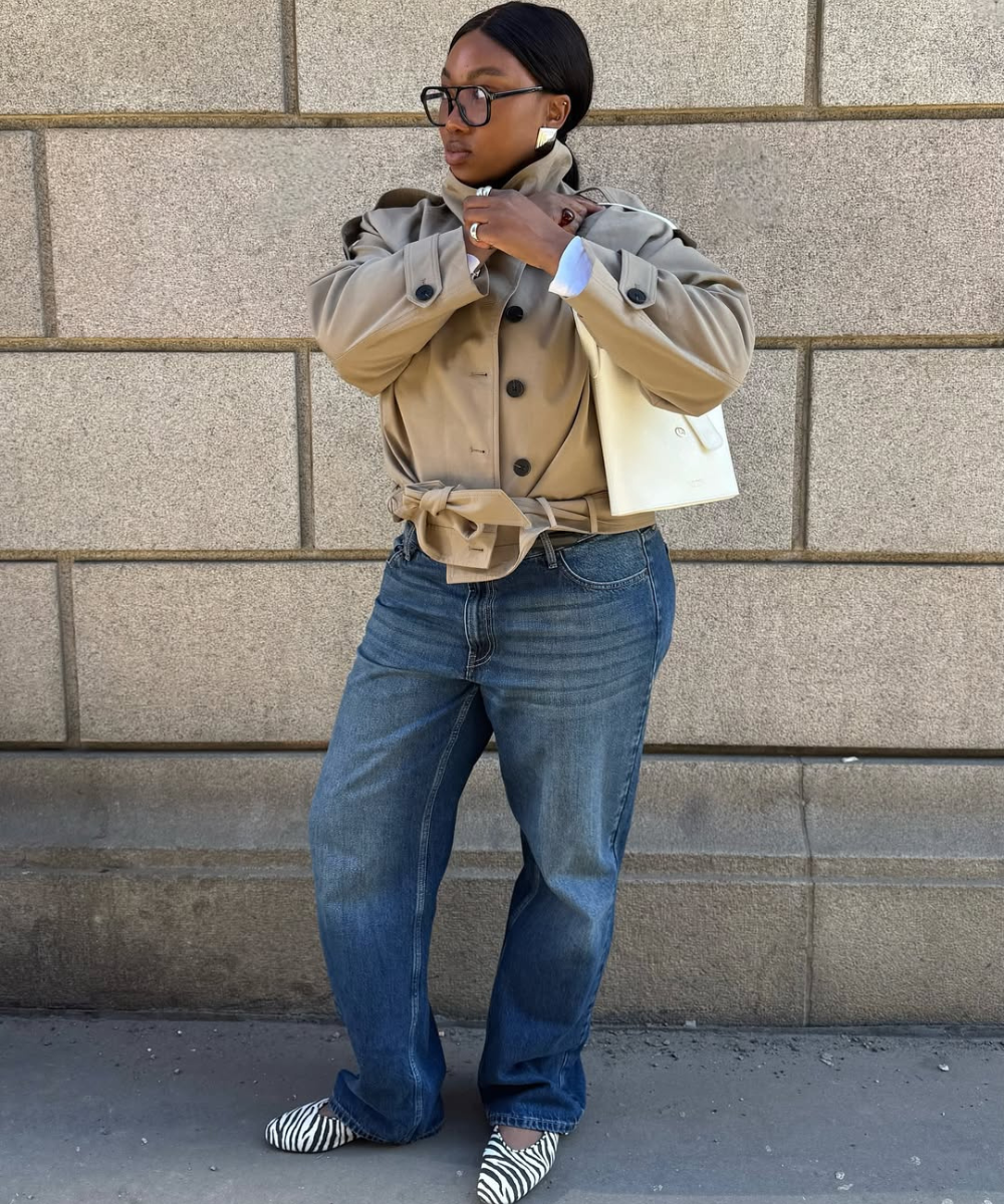 Modelo posa com jaqueta bege de botões e cinto, jeans azul largo e sapatos estampados tendência em zebra, criando look