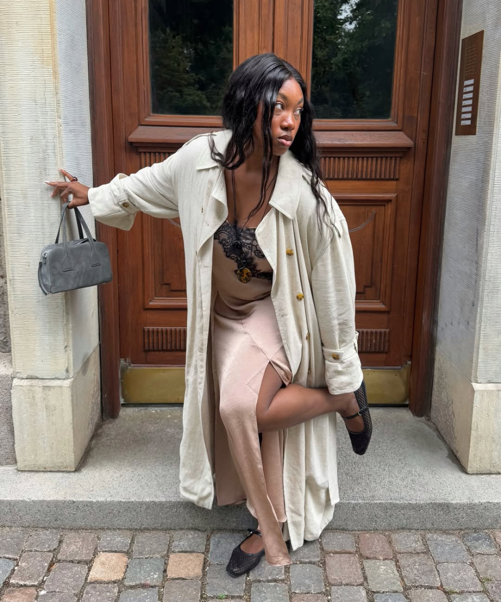 Modelo ajusta sapatos femininos estilosos em tecido texturizado preto com tiras, usando vestido rosa acetinado e casaco bege