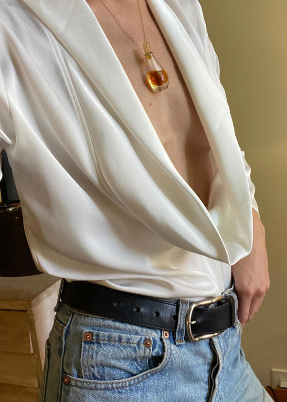 Colar funcional em vidro com líquido âmbar destaca-se sobre blusa branca de seda com decote profundo e jeans azul claro,