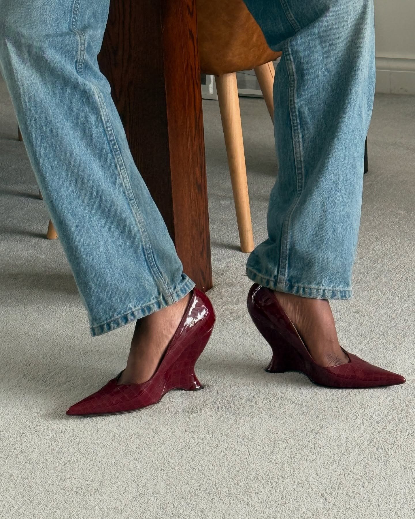 Scarpin clássico em verniz bordô com textura croco e salto escultural, combinado com jeans azul claro para um visual moderno
