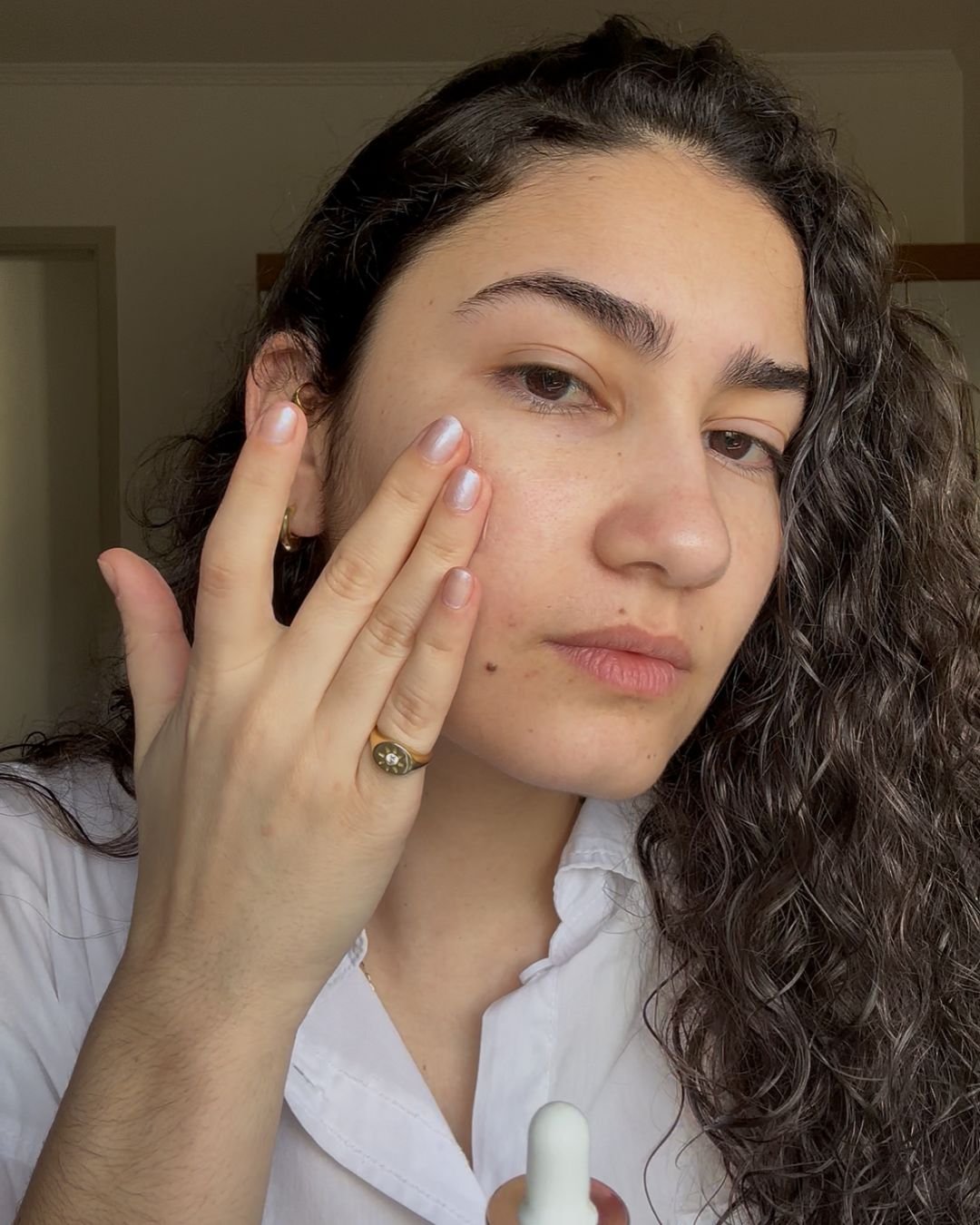 Mulher aplicando sérum facial, destacando a textura da pele e a rotina de cuidados.