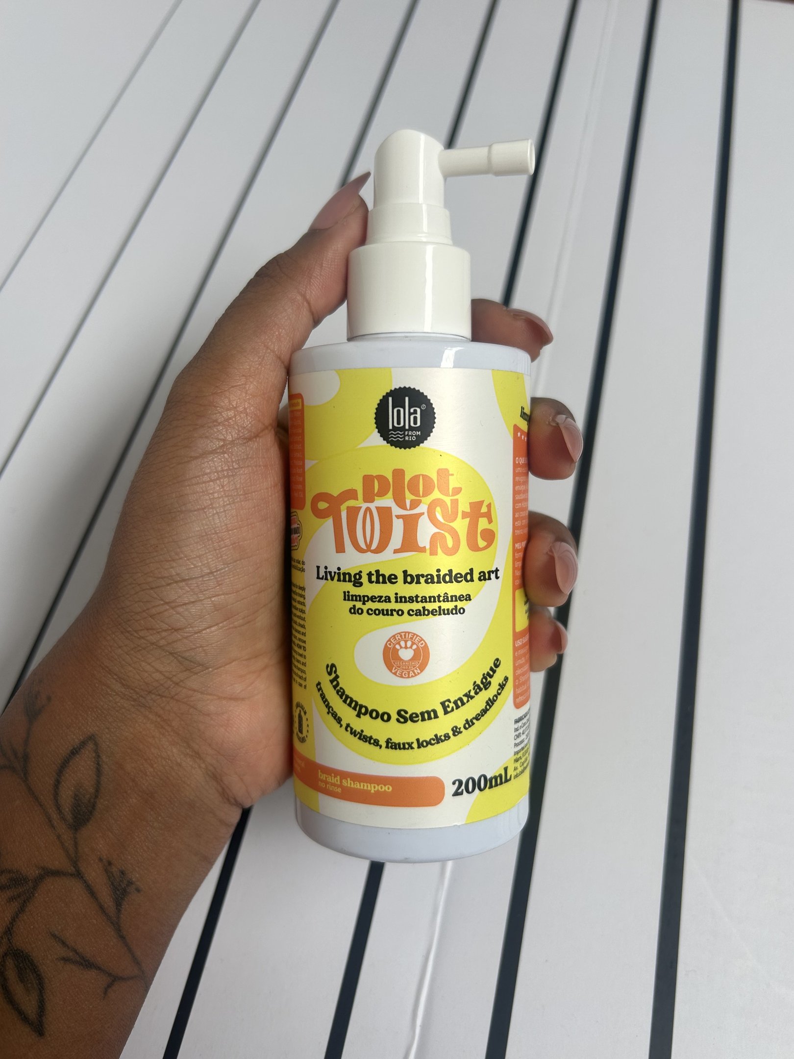 Mão  segura frasco branco e amarelo de shampoo para trança sem enxágue, com design vibrante.