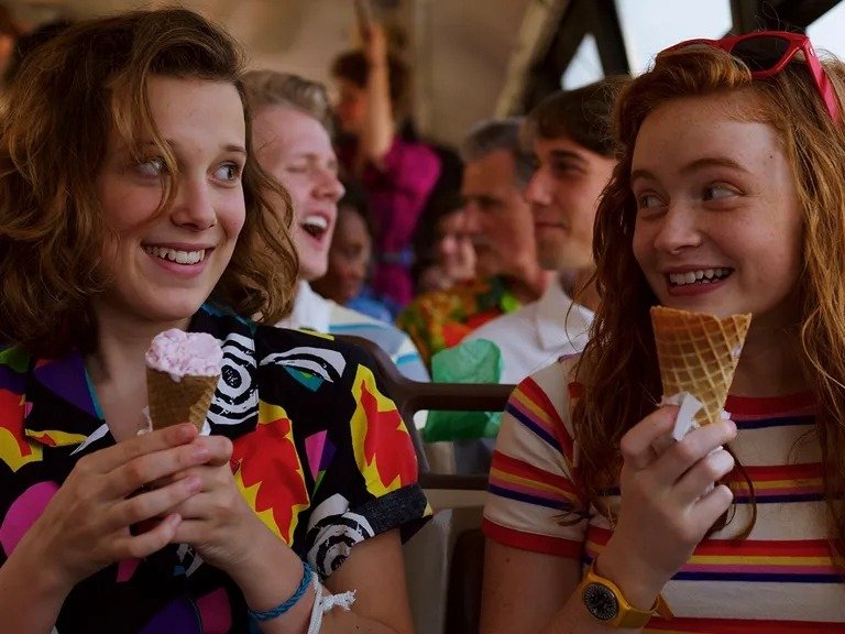 Duas jovens sorriem segurando sorvetes, com roupas vibrantes e listradas que refletem tendências de moda e beleza alegres e