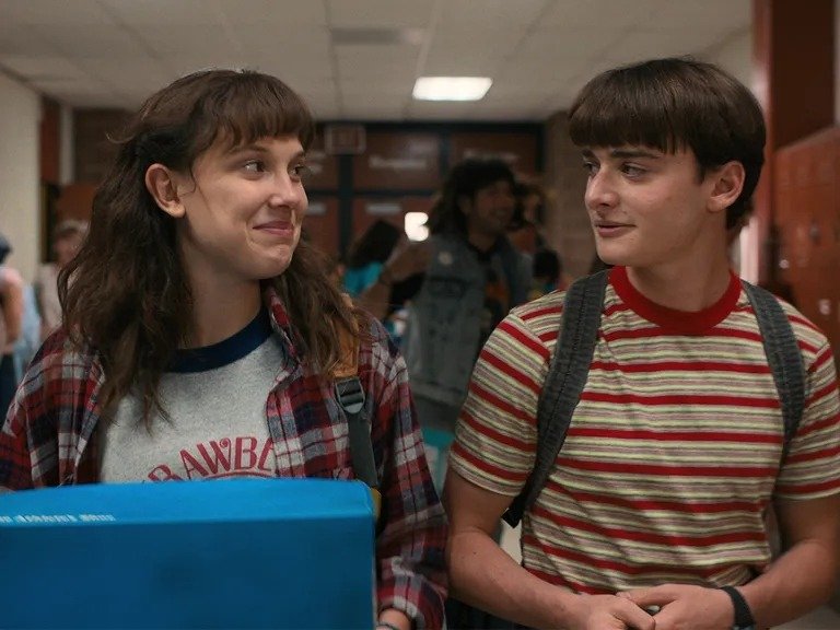 Adolescentes vestem peças casuais com camisetas listradas e xadrez em tons terrosos, refletindo tendências de moda e beleza