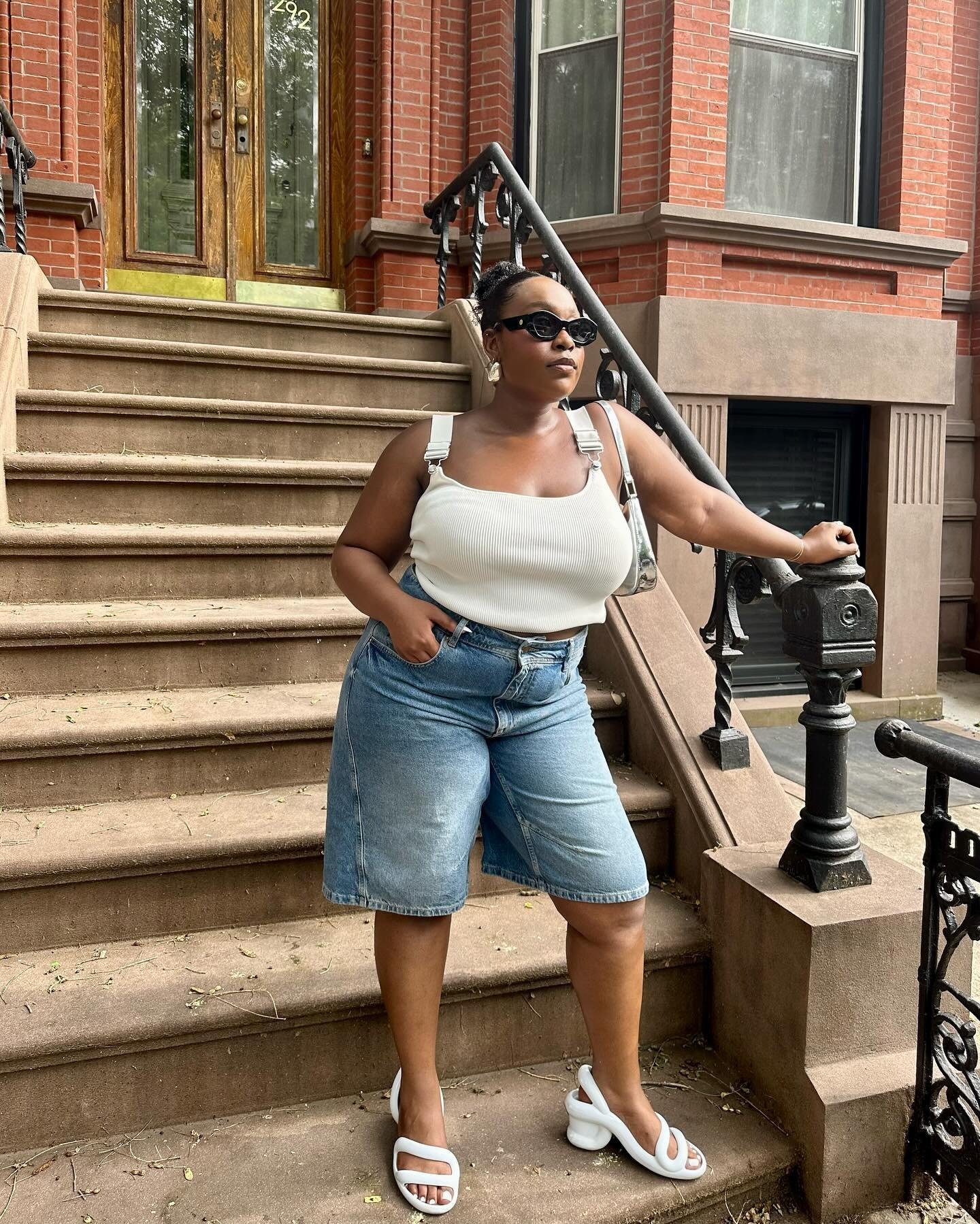 A imagem apresenta uma mulher em uma escadaria, usando um top branco e shorts jeans. Os sapatos, descritos como