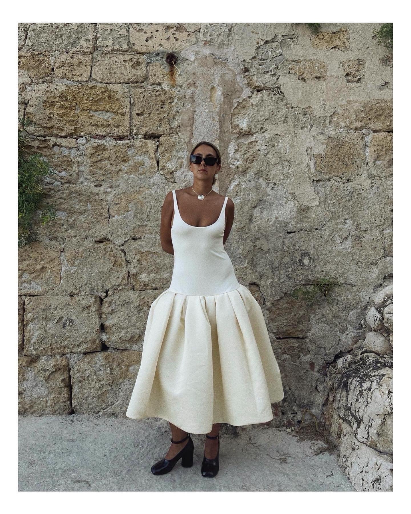 Vestido branco com modelagem justa no corpo e saia volumosa em tecido estruturado, combinando elegância e conforto para