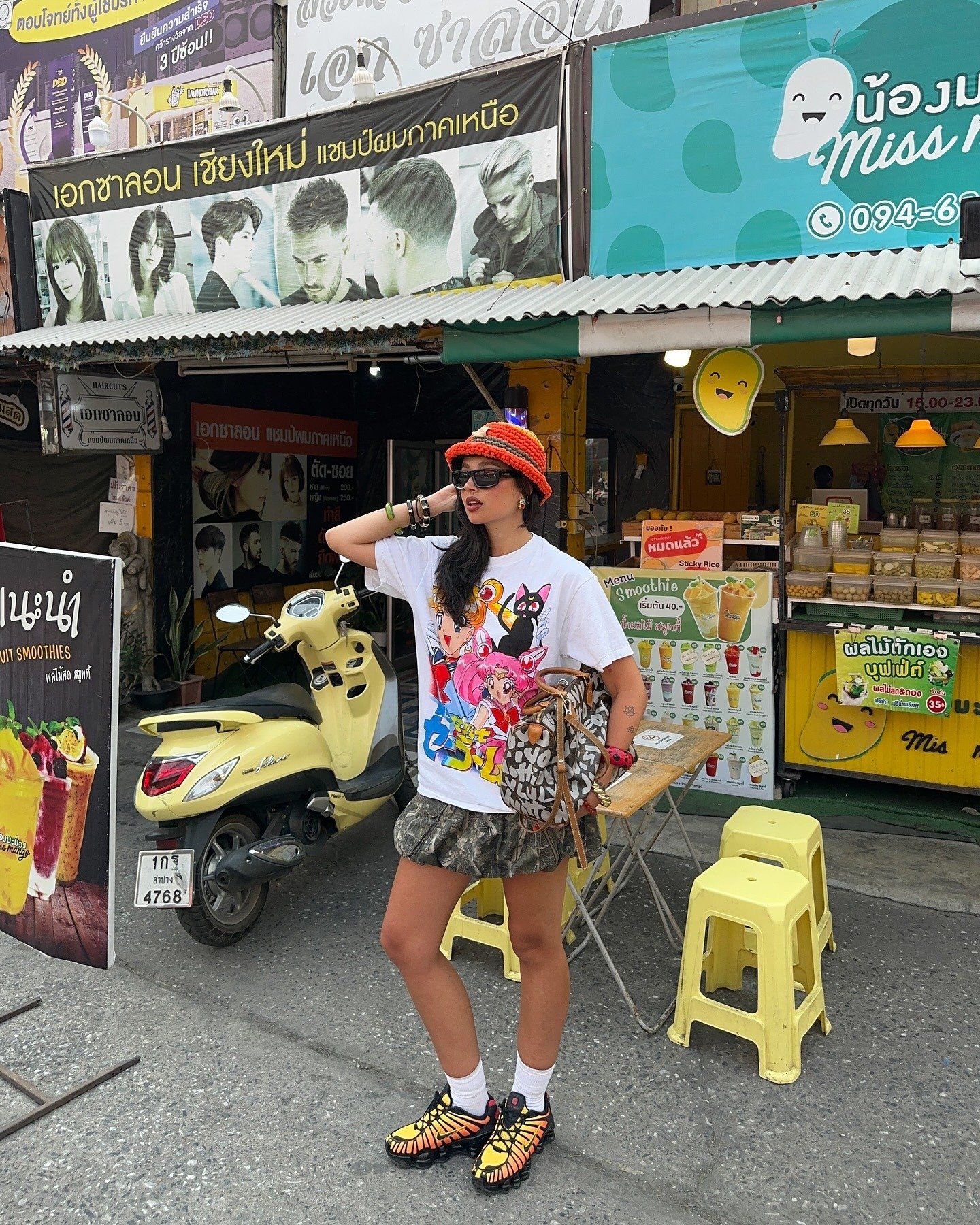 A imagem apresenta uma jovem em um ambiente urbano vibrante, usando um tênis polêmico com design arrojado. Ela veste uma camiseta estampada com personagens coloridos, uma saia camuflada e acessórios que complementam seu estilo ousado.