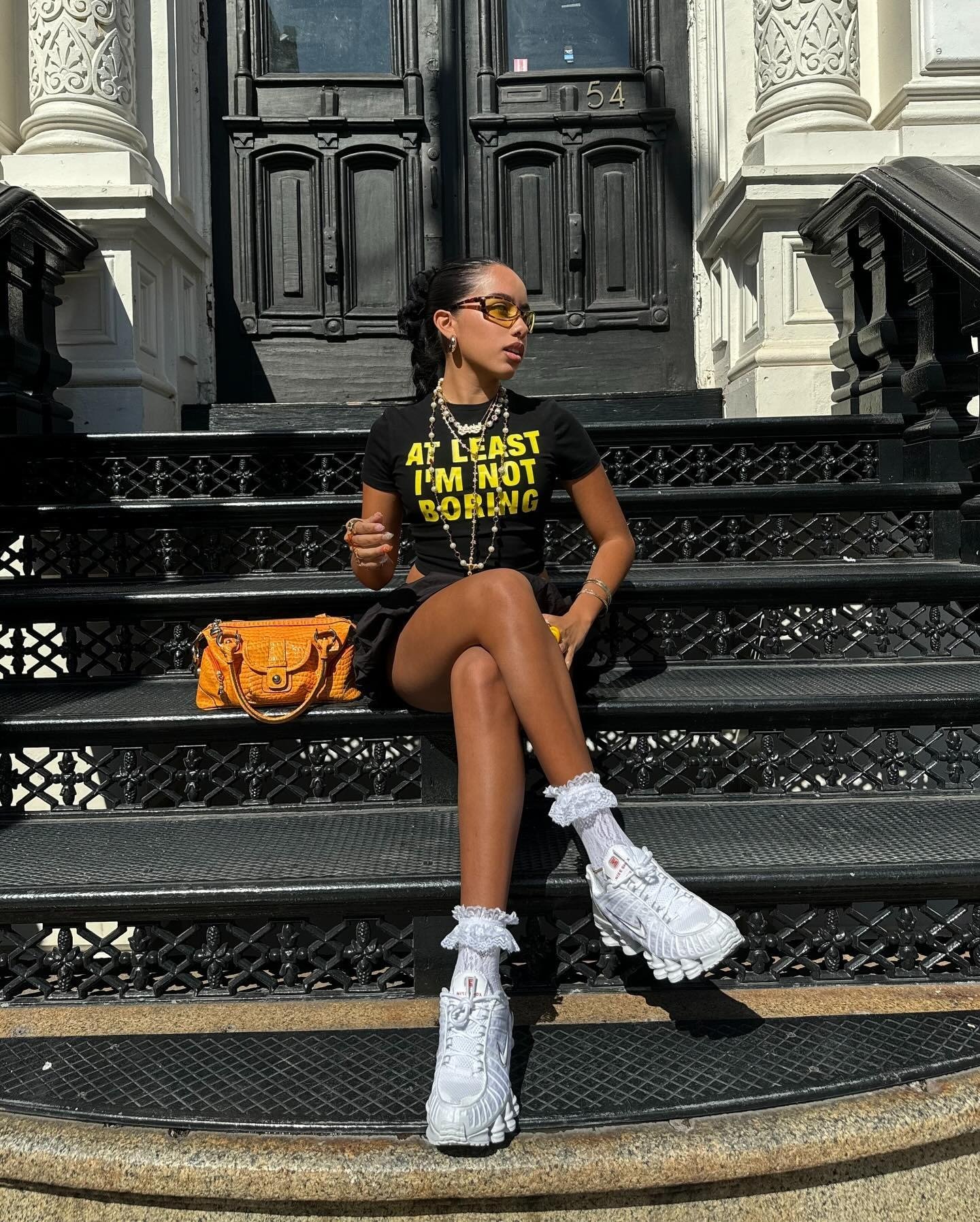 Look ousado com tênis polêmico e estilo contemporâneo. A combinação de camiseta com frase impactante, saia e acessórios cria um visual marcante. O tênis, em destaque, traz um toque esportivo e inovador, ideal para quem busca se destacar na moda urbana.