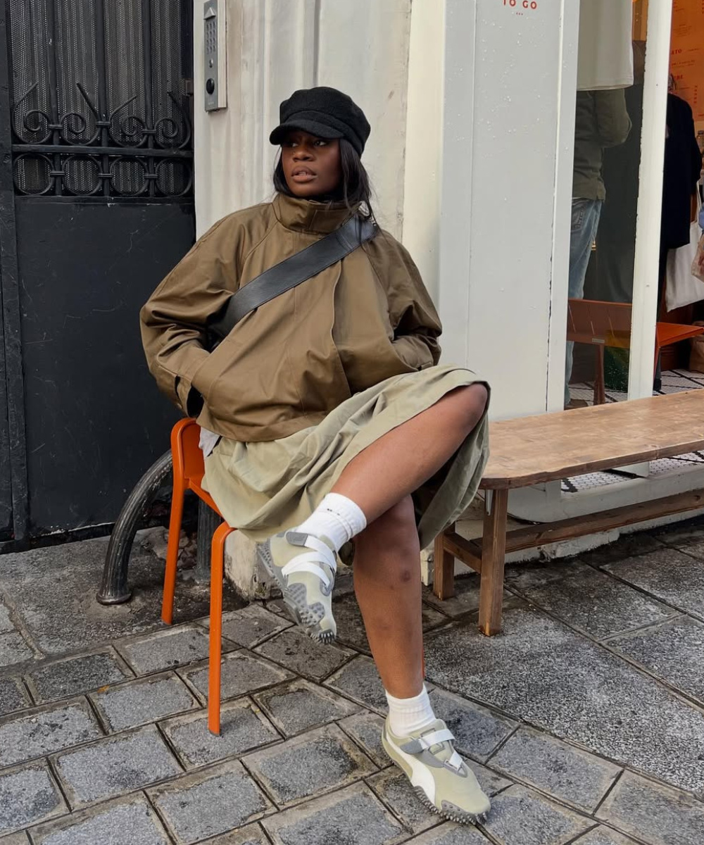 Modelo senta com postura relaxada usando tênis tendência de 2026 em tons neutros com velcro, combinando com jaqueta