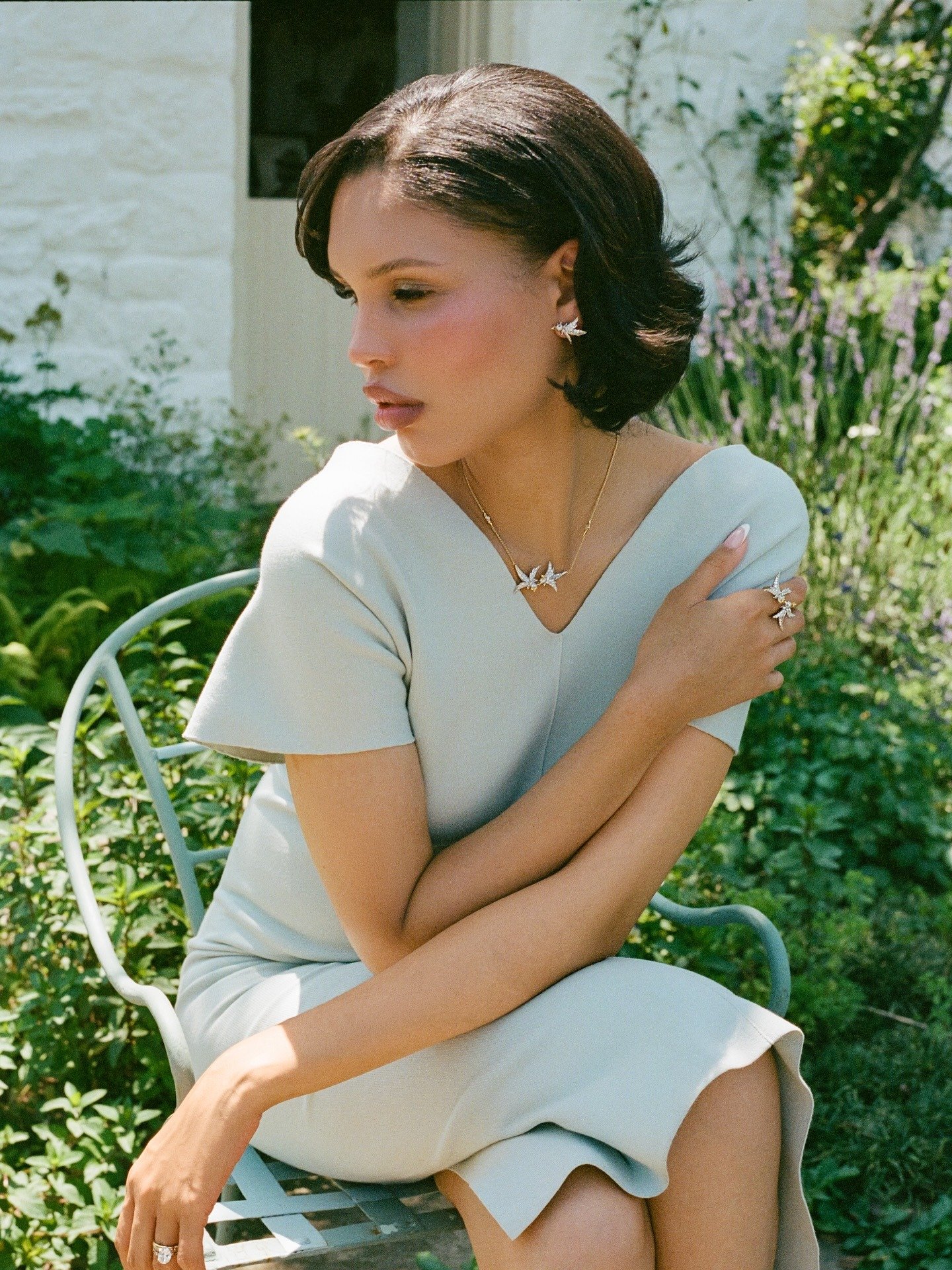 Mulher sentada em jardim veste vestido azul claro de tecido estruturado com mangas curtas e decote em V, tradwife.