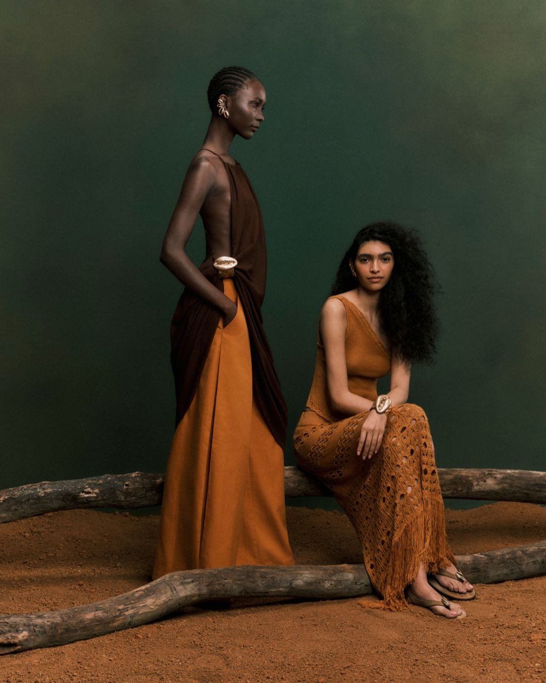 Duas modelos em trajes de tricô no verão, com tons terrosos, destacam a leveza e a elegância do tricô no verão. O cenário minimalista realça as texturas e detalhes das peças, como franjas e padrões vazados, sugerindo um estilo sofisticado e fresco.