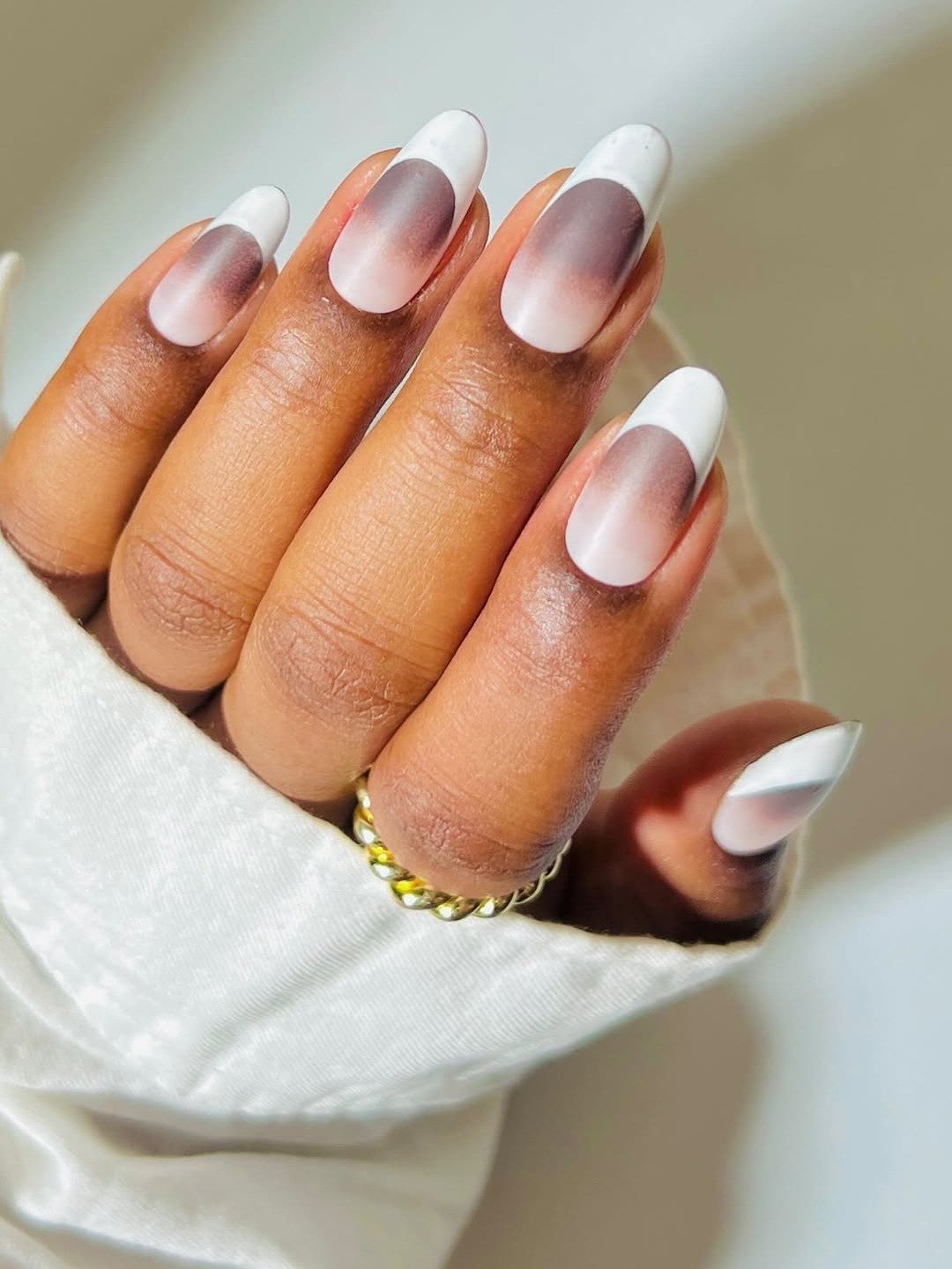 Unhas com esmalte fosco em degradê nude e branco, formato oval, transmitindo delicadeza e sofisticação minimalista.