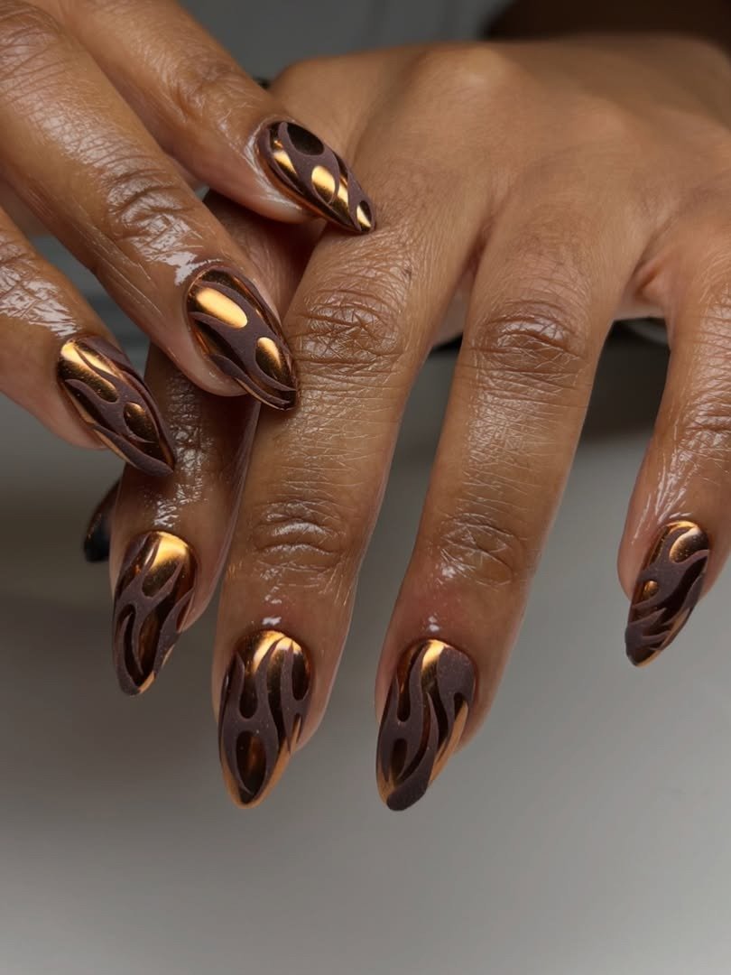 Unhas longas com esmalte fosco marrom e detalhes flamejantes em dourado metálico criam estilo marcante e sofisticado.
