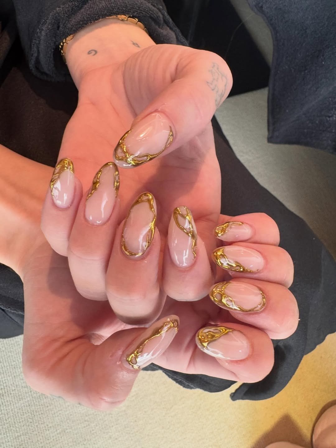 Unhas para o natal e ano novo em formato amendoado com base nude e detalhes dourados que transmitem elegância e sofisticação.