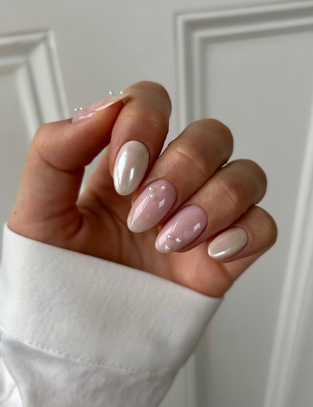 As unhas para o Ano Novo apresentam um design elegante, com uma combinação de tons nude e rosa claro. Algumas unhas possuem um acabamento brilhante, enquanto outras são decoradas com pequenas pérolas, conferindo um toque sofisticado.