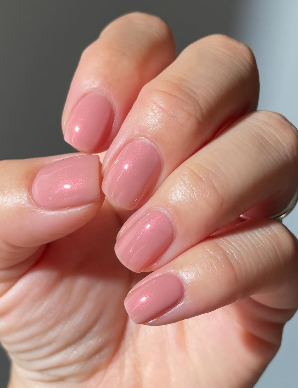 Unhas para o Ano Novo em tom rosa claro apresentam um acabamento brilhante e elegante. A manicure destaca a suavidade do esmalte, refletindo luz de forma sutil.