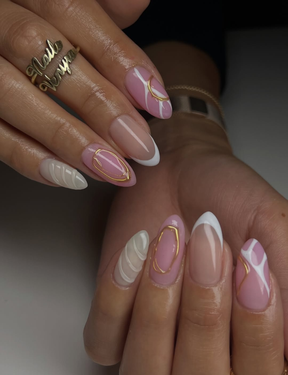 Unhas para o Ano Novo apresentam um design elegante e sofisticado. As unhas são em formato stiletto, com uma combinação de esmaltes em tons de rosa, nude e branco. Detalhes em dourado, como linhas e formas geométricas, adicionam um toque glamouroso.