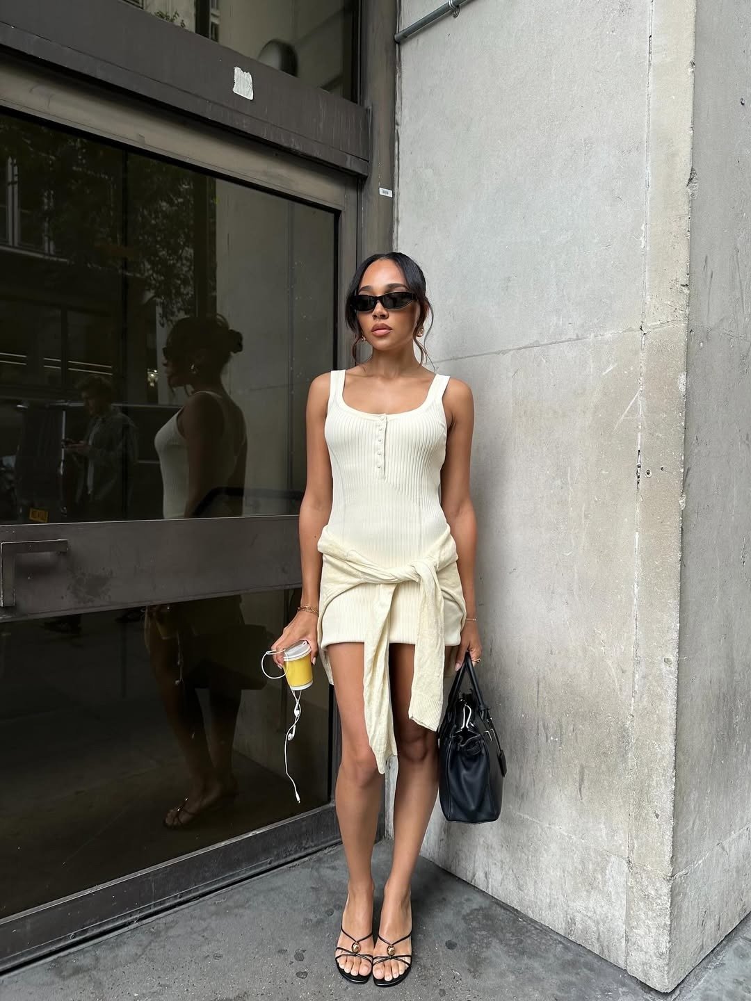 Modelo posa com vestido feminino curto canelado off-white, amarração na cintura, sandálias pretas e bolsa estruturada.