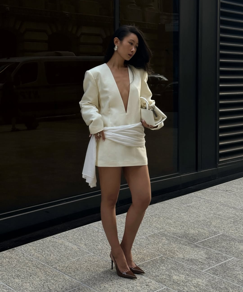 Um vestido branco curto, com decote profundo e mangas largas, destaca-se como uma escolha moderna para o Réveillon. A peça possui um detalhe de drapeado na cintura, conferindo elegância.