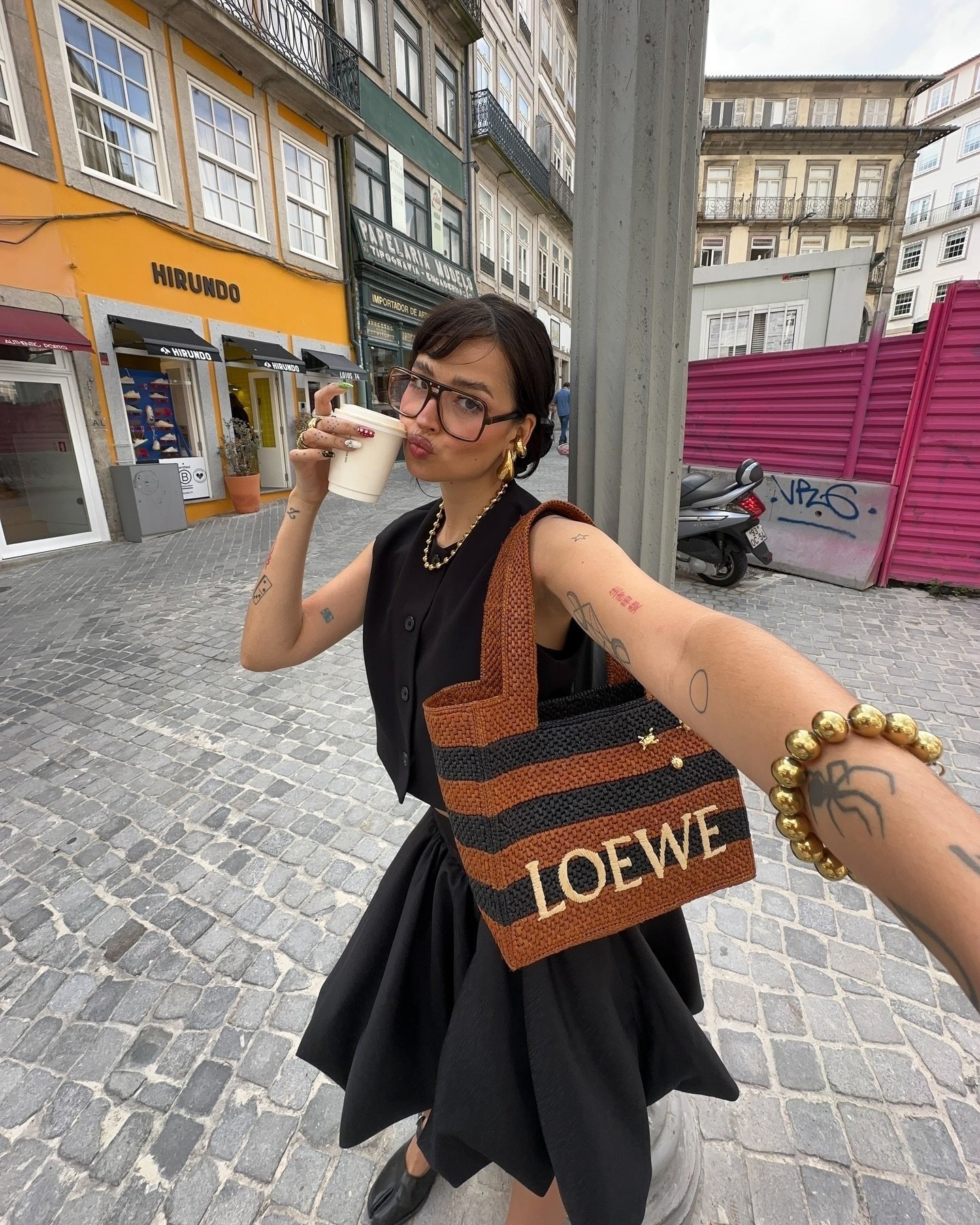 Modelo posa com acessórios que vão bombar em 2026: bolsa de crochê listrada marrom e preta, maxi brincos e pulseira dourada,