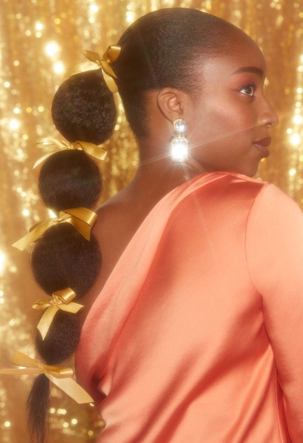 Modelo posa com penteado de Natal fácil em rabo de cavalo dividido por cinco bolas volumosas presas por laços dourados,