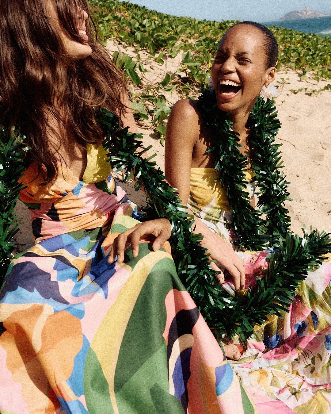 guia do amigo secreto - com vestidos longos de tecido leve e estampas coloridas vibrantes, modelo ri e posa alegre na praia