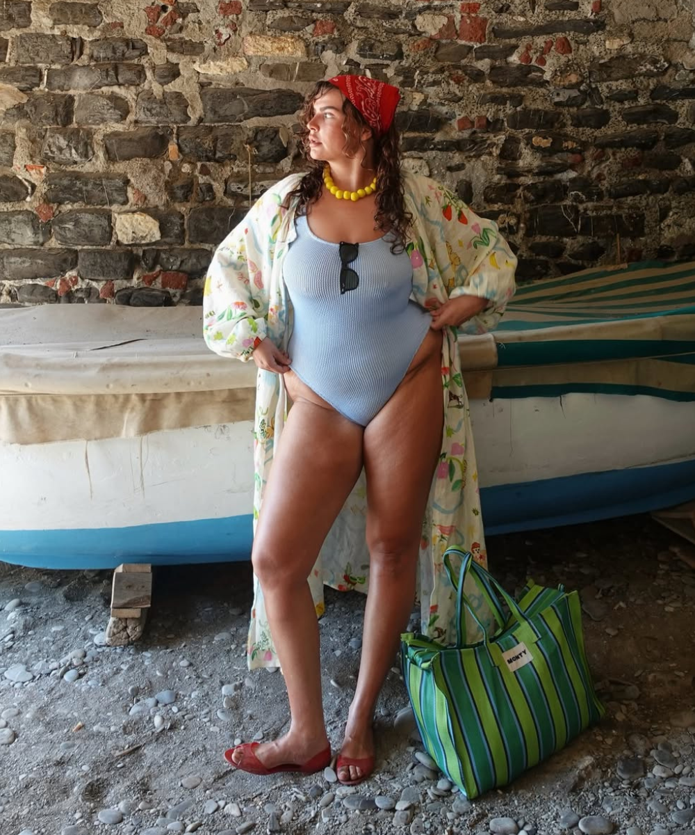 Modelo posa com maiô azul claro, quimono estampado leve, sandálias vermelhas e bolsa para praia listrada verde.