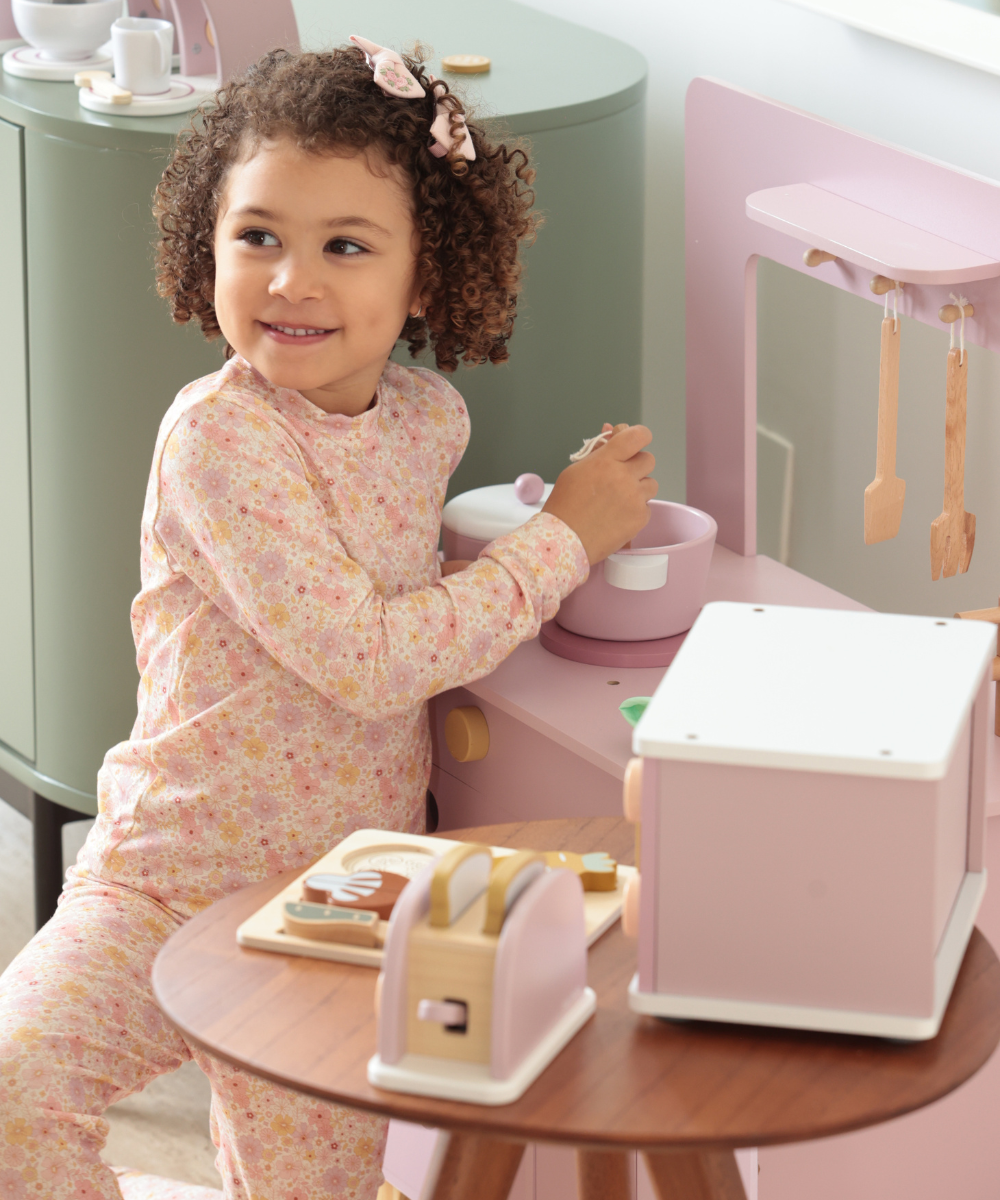 Brinquedos de madeira em tons neutros e pastel compõem cenário acolhedor com café e doces artesanais simulados.