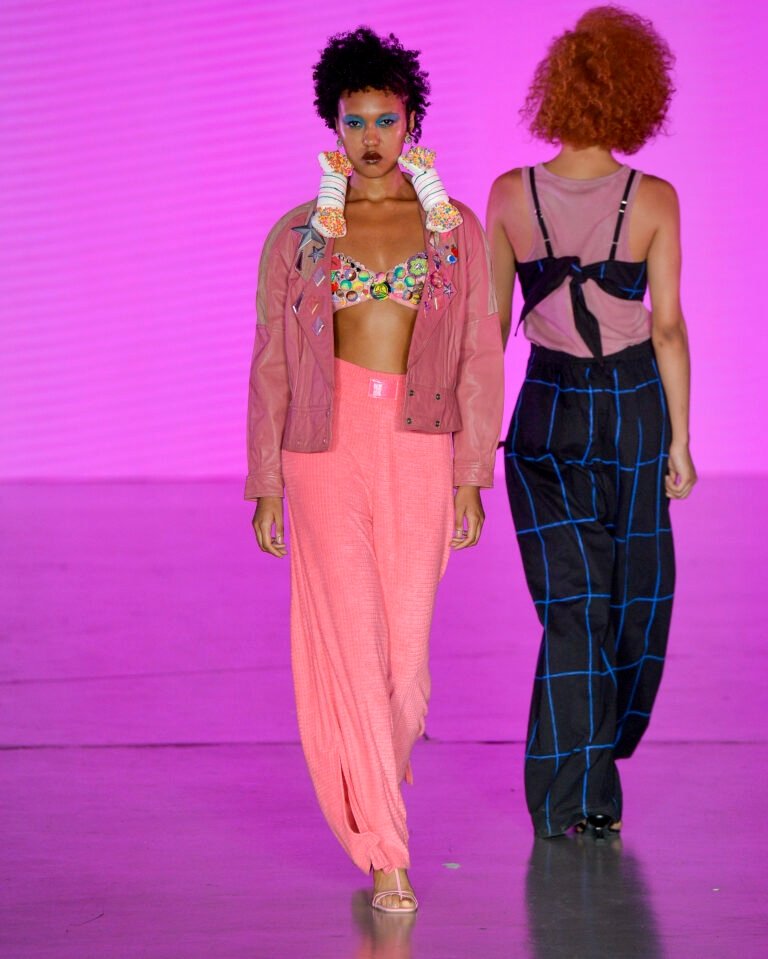 Modelo da casa de criadores 57 desfila com jaqueta rosa, top colorido bordado, calça larga rosa e acessórios volumosos, em