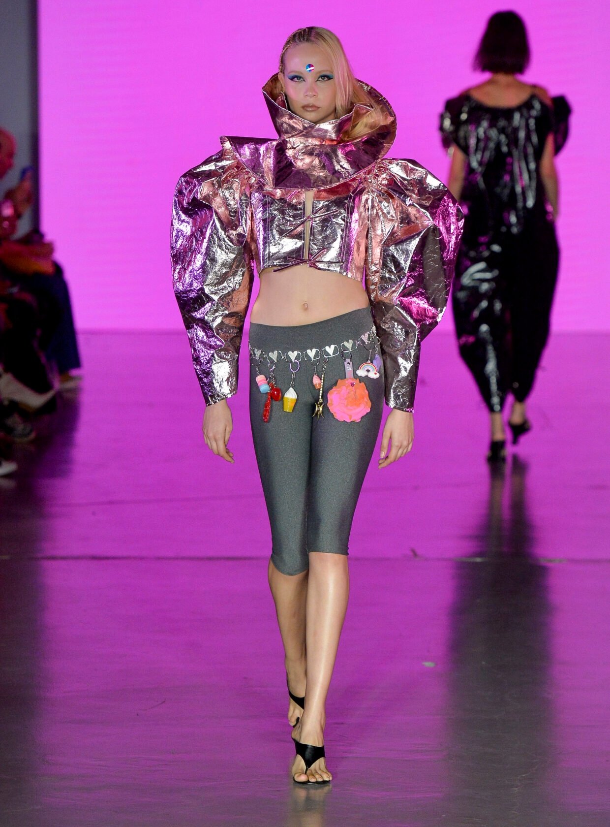 Modelo caminha com postura confiante na casa de criadores 57 usando cropped metálico rosa com mangas volumosas e legging