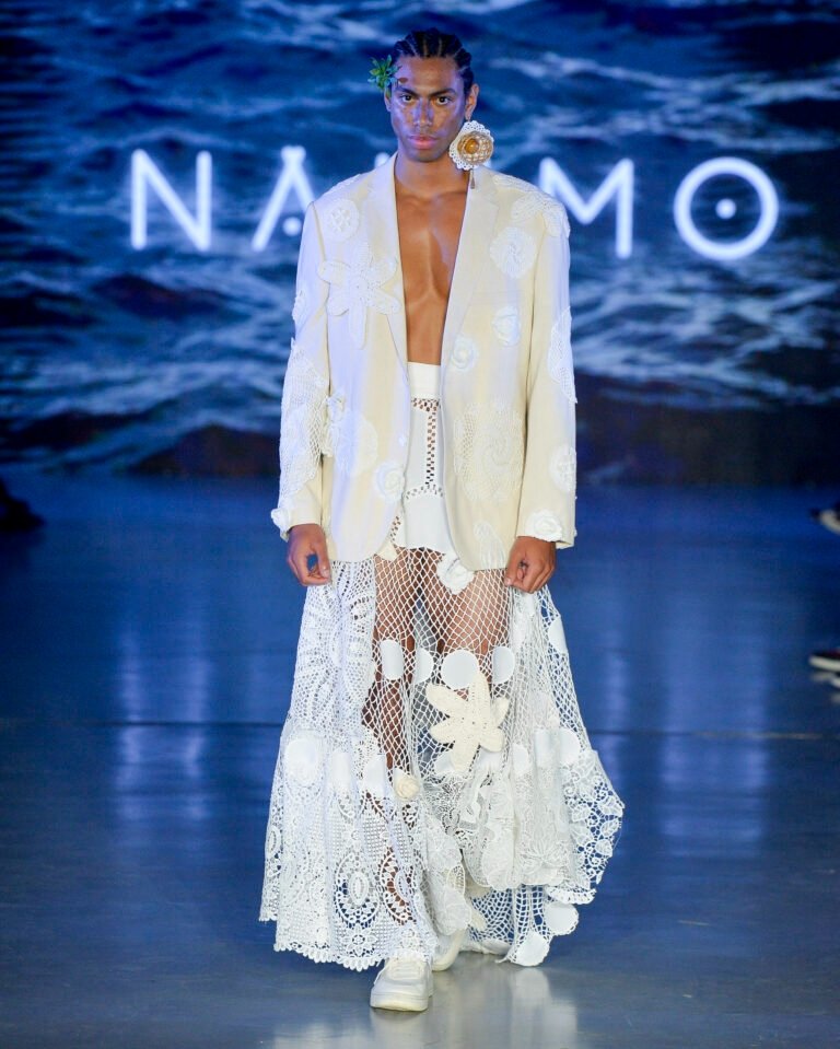 Modelo caminha com blazer off-white bordado e saia longa de renda e tule com aplicações florais, criando visual etéreo na