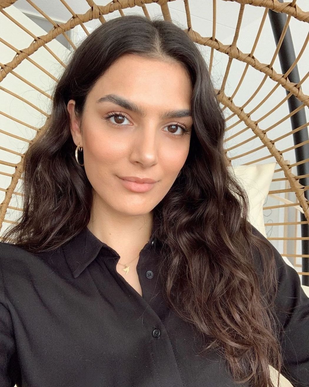 Modelo posa com camisa preta de algodão e cabelo ondulado solto, evidenciando como cuidar do cabelo ondulado.