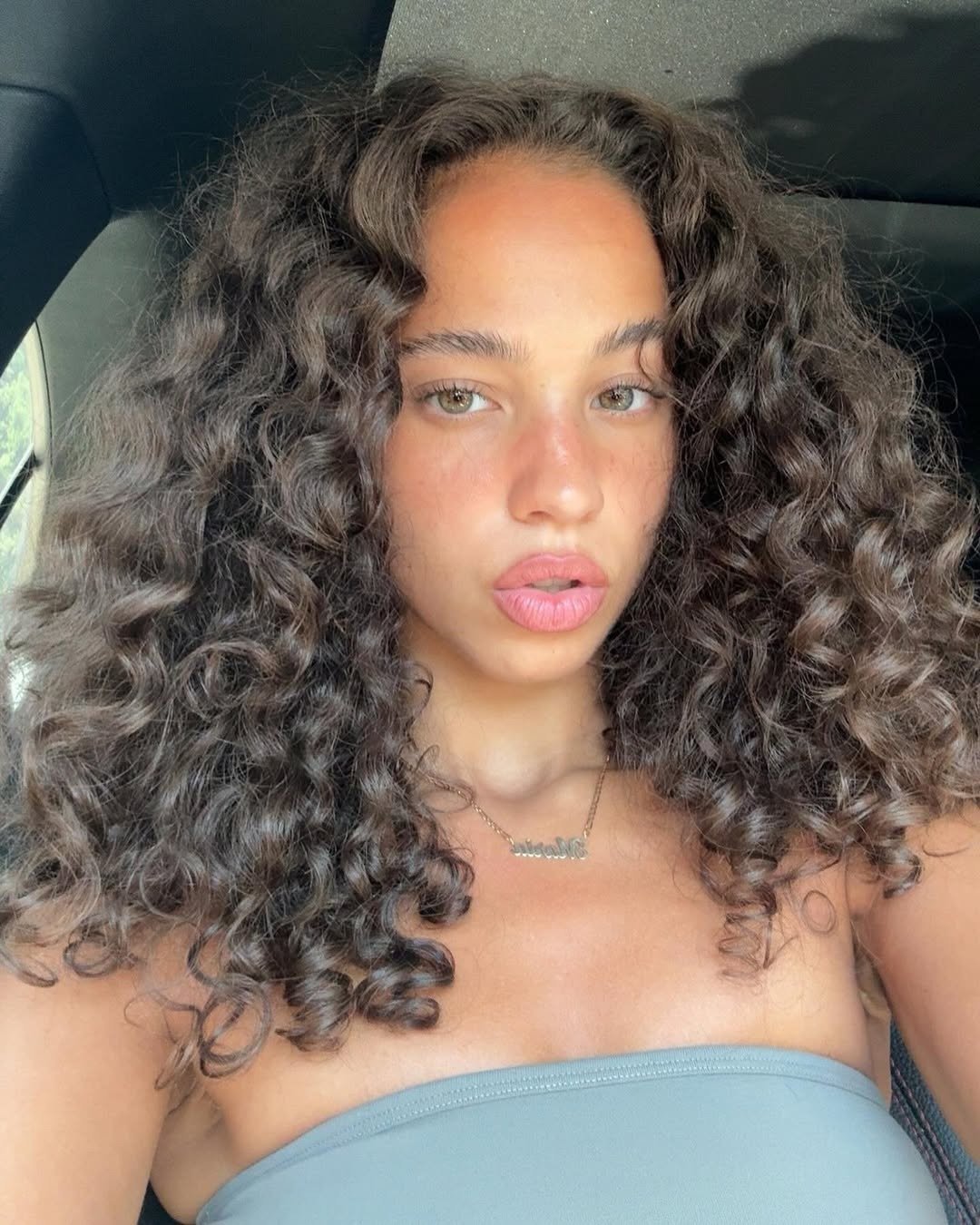 Modelo posa com cabelo ondulado volumoso e definido, usando top cinza de tecido liso, em clima natural e confiante.