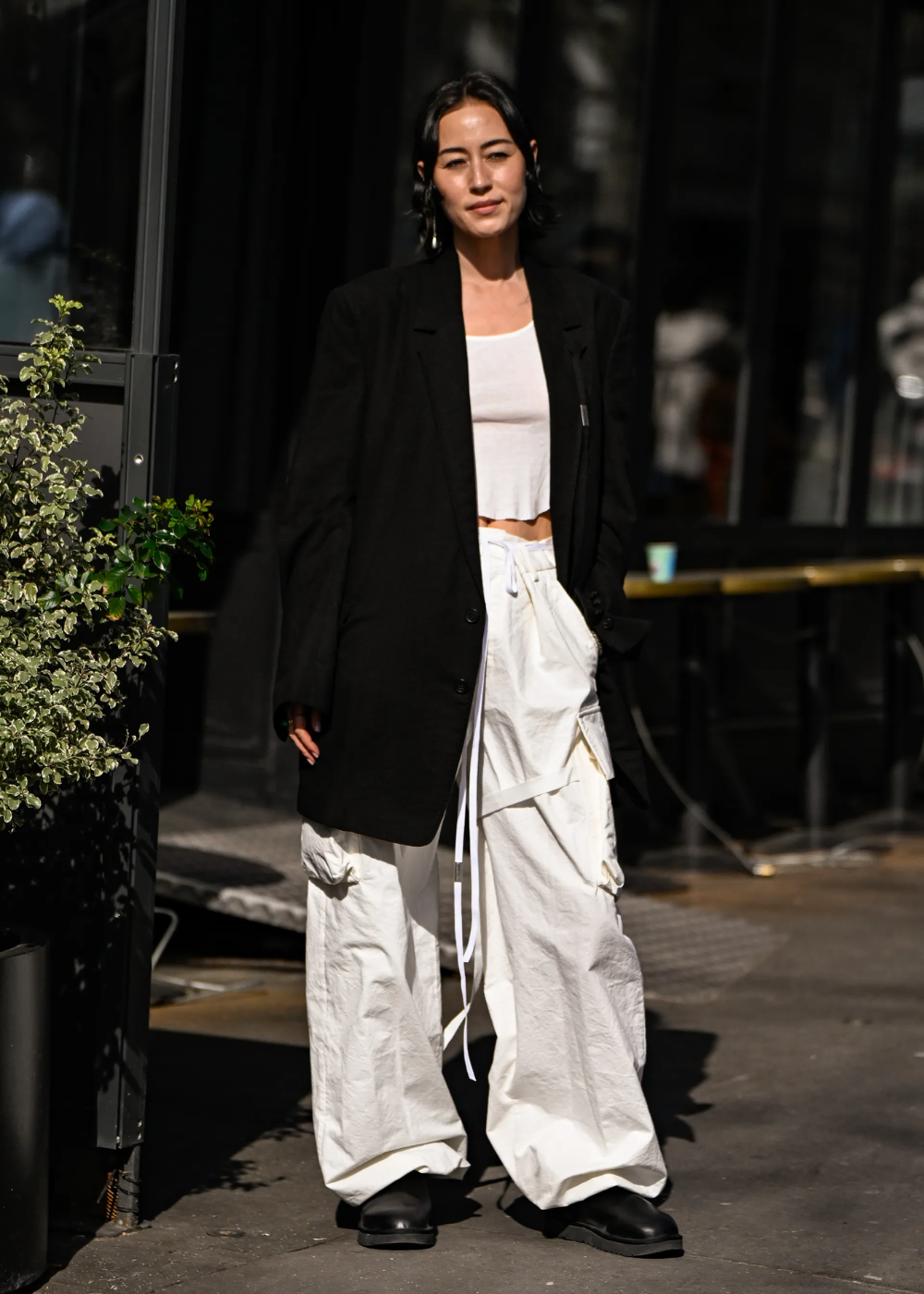 Modelo posa com calça cargo branca de tecido leve e bolsos laterais amplos, combinada a blazer preto oversized e cropped.