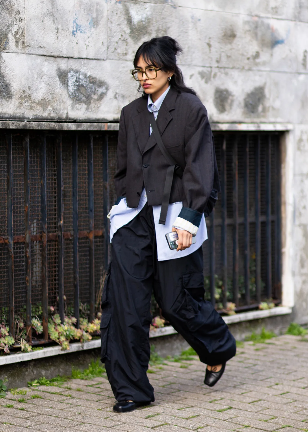 Modelo caminha com postura confiante usando calça cargo preta de tecido leve e bolso lateral, combinada com camisa azul.