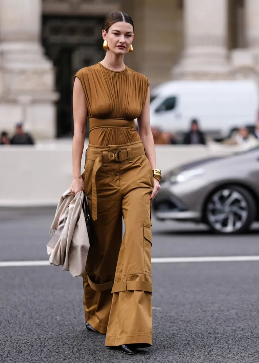 Modelo caminha com postura confiante usando calça cargo ampla caramelo com bolsos laterais e cinto largo, combinada a blusa.