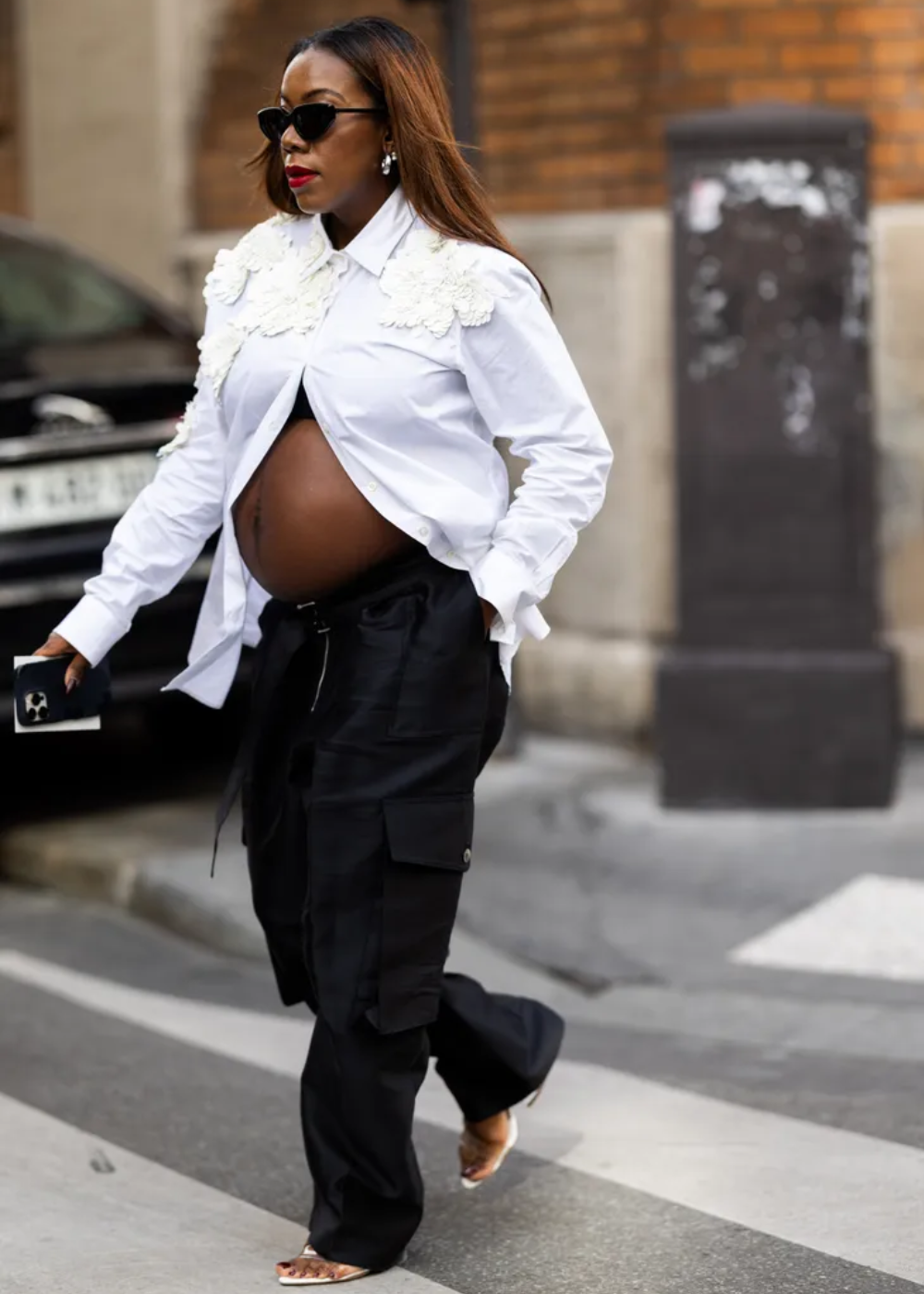 Modelo grávida caminha confiante com calça cargo preta de tecido leve e bolsos laterais, combinada a camisa branca.