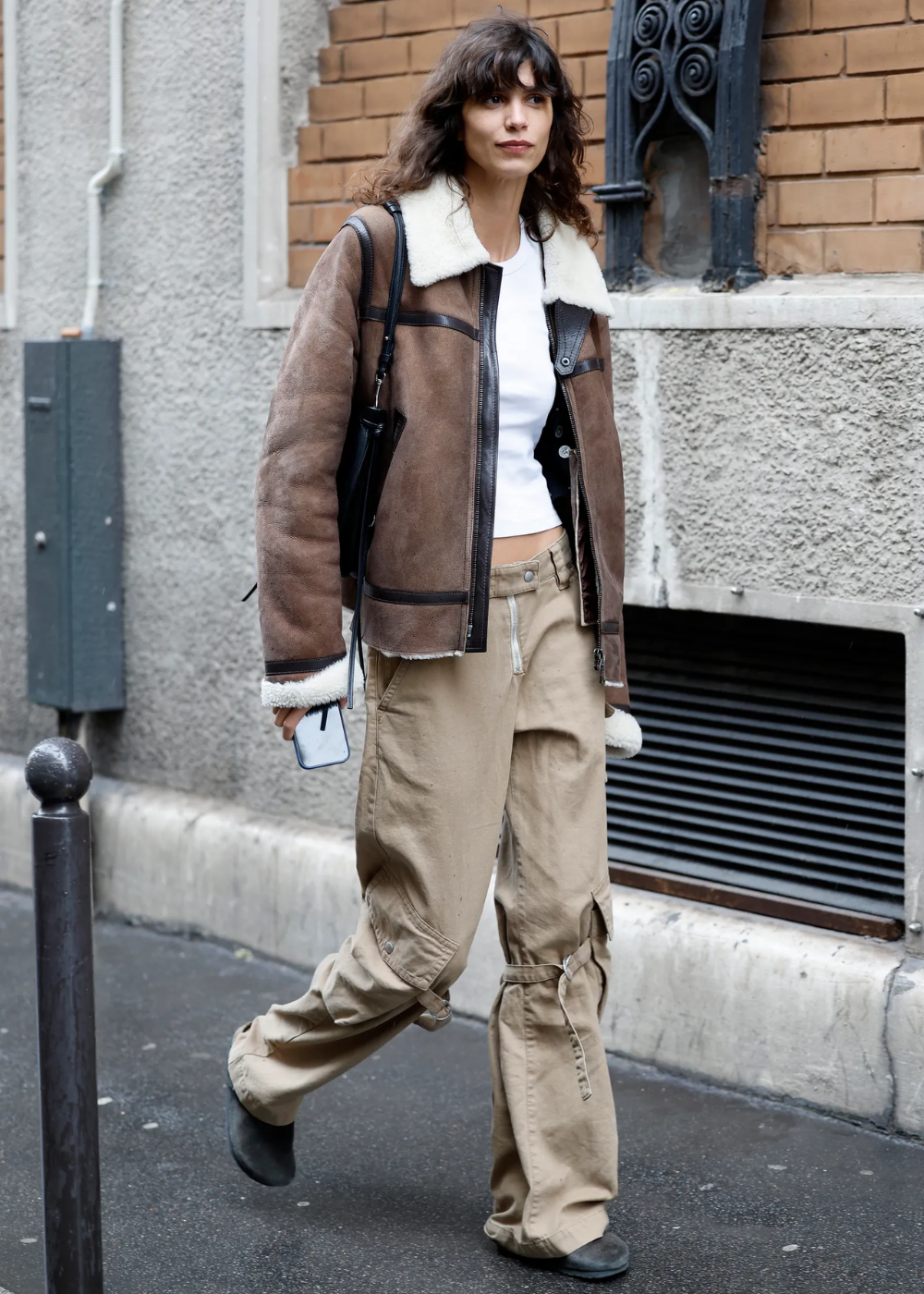 Modelo caminha confiante usando calça cargo bege de algodão com bolsos laterais e tiras, combinada a jaqueta marrom de couro.