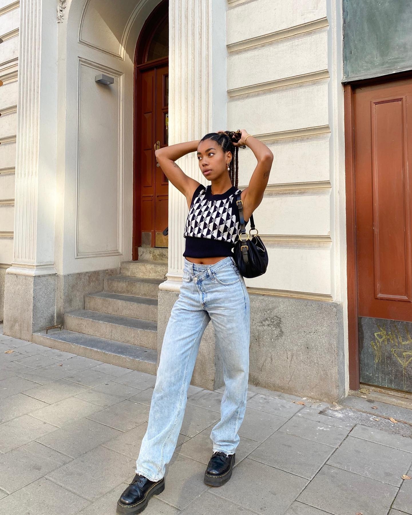 Modelo posa com postura confiante usando jeans claro de cós transpassado, top cropped preto e branco e sapatos pretos