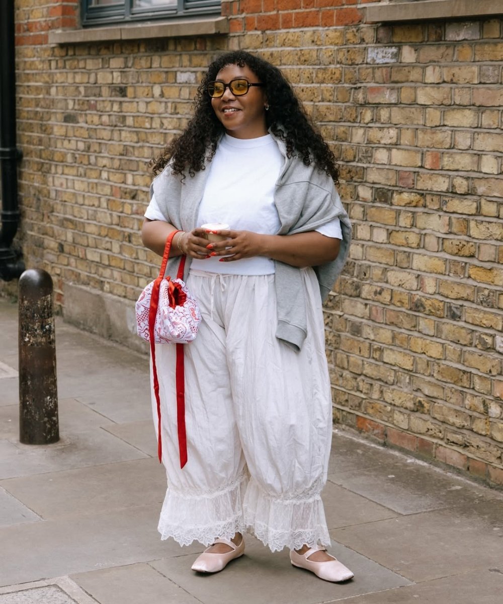 Modelo posa sorridente com a calça mais cool do momento em tecido leve branco, modelagem ampla e barra rendada, combinada a