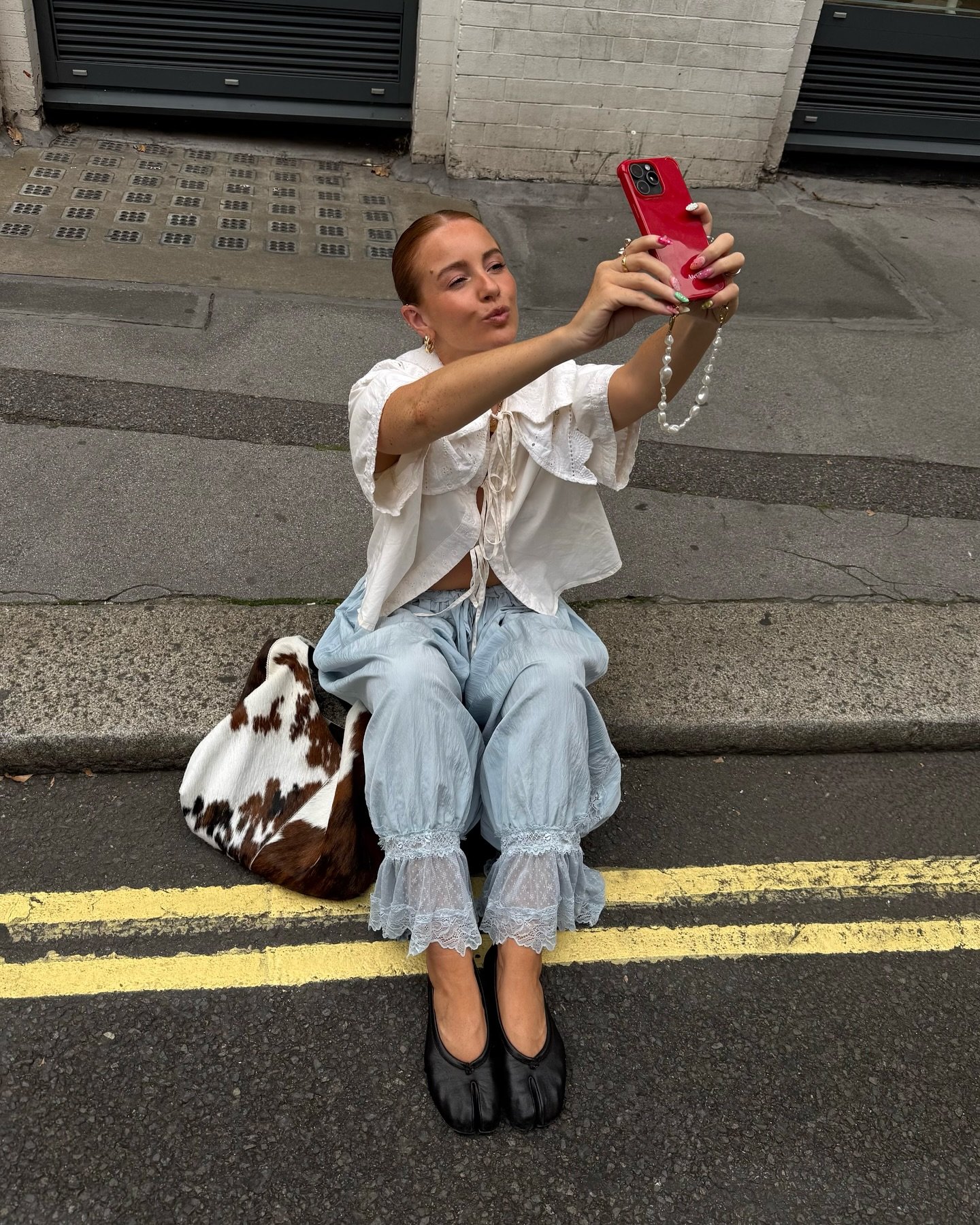 Modelo senta no meio da rua e posa para selfie usando a calça mais cool do momento, azul clara com babados e renda na barra,