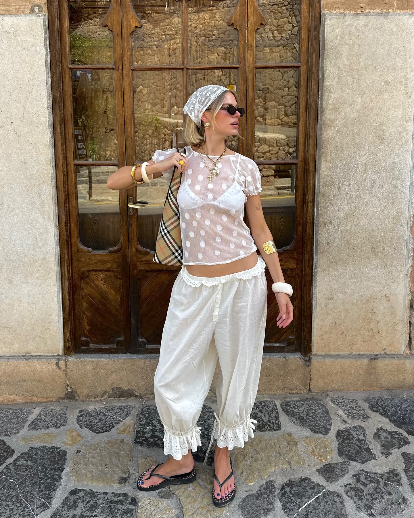 Modelo posa com a calça mais cool do momento, ampla de tecido leve branco com babados rendados na barra, combinada a blusa